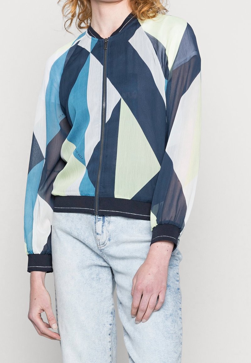 Giacca bomber colorata con un motivo geometrico in blu, blu navy e verde, realizzata in tessuto leggero con polsini e orlo neri.