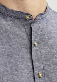 Camicia button-up con colletto in lino blu scuro, caratterizzata da bottoni simili a perle e una sottile texture. In evidenza il collo e la disposizione dei bottoni.