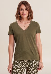 T-shirt verde oliva a V, realizzata in tessuto morbido. Maniche corte con un design semplice, caratterizzata da un sottile dettaglio di cucitura sul colletto.