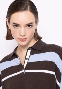 Brązowy, dziany polo z poziomymi niebieskimi i białymi paskami, z klasycznym kołnierzykiem i zapięciem na dwa guziki. Gładka tekstura i dopasowany krój.