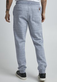 Grå, teksturerte joggebukser med en smal passform, elastisk livlinning og en baklomme, sammen med svarte sneakers.