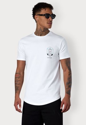 T-shirt en coton blanc avec un col rond et des manches courtes, avec un imprimé coloré sur la poitrine et un pantalon noir.