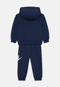 Tumed sinine kapuutsiga särk ja jogger komplekt, mis on valmistatud pehmest kangast. Omab känguru taskut, soonikkraede ja silmapaistvat valget logot pükste sääre peal.