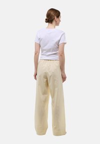 T-shirt blanc à manches courtes porté avec un pantalon large à rayures jaunes et blanches, doté d'une taille élastique et d'une coupe décontractée.