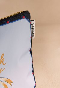 Ljusblå påse med guldfärgad dragkedja, svart och blå kant, röda stjärndetaljer och en vit etikett med texten "Cath Kidston" på sidan.