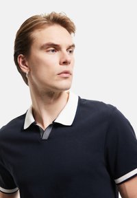 Merihenkinen polo paita, jossa on valkoinen kaulus ja raidallinen yksityiskohta. Lyhyet hihat valkoisilla yksityiskohdilla. Pehmeä, sileä kangas ja klassinen istuvuus.