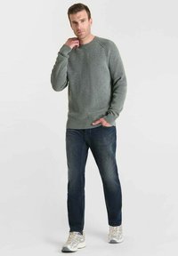 Hellgrauer gestrickter Pullover mit gerippten Bündchen und Saum, kombiniert mit dunkelblauen Jeans und hellen Sneakern. Lässige Passform, strukturiertes Material.