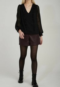 Černá průsvitná blůza s volány, spárovaná s burgundskými koženými šortkami, punčochami s puntíky a černými šněrovacími botami.