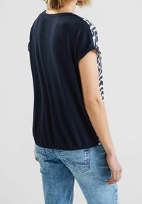 Haut navy à manches courtes avec un panneau latéral à motifs, en tissu doux et coupe décontractée. Associé à un jean en denim bleu clair.