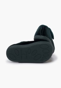 Pantofola in velluto con forma arrotondata, di colore verde scuro, suola in gomma con motivo testurizzato e un accento a fiocco sulla parte superiore.
