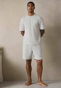 Helles graues Baumwoll-T-Shirt und Shorts-Set mit weichem Griff, lockerer Passform und leicht fallenden Schultern, das ein minimalistisches Design aufweist.