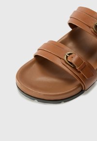 Brune faux lær sandal med to brede stropper og en messinglås detalj. Flat såle med en teksturert svart bunn for grep.