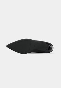 Black high-heeled shoe with a pointed toe, crafted from soft suede. The sole is smooth, featuring a slight tread for grip.