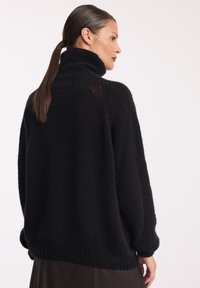 Czarny, oversize sweter z wysokim kołnierzem, o fakturowanej tkaninie, z opadłymi ramionami, ribbrowanymi mankietami i dołem, w luźnym fasonie.