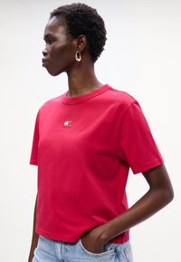 Rød bomulds t-shirt med rund hals, kortærmede, og et lille logo-lap. Bæret med lyseblå denim shorts. Glat tekstur.