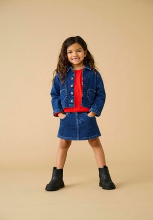 Denim jack met hartvormige zakken, gecombineerd met een rode t-shirt en denim rok. Zwarte enkellaarsjes maken de outfit af.