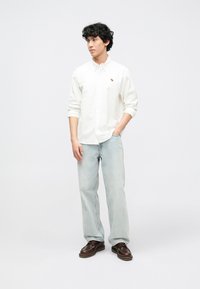 Λευκό πουκάμισο με κουμπιά, ανοιχτό μπλε τζιν παντελόνι και καφέ παπούτσια με κορδόνια. Το πουκάμισο έχει μικρή κεντητή ζωγραφιά ζώου στο στήθος.