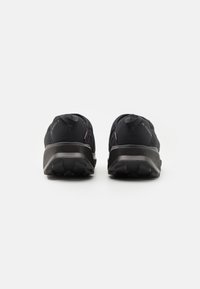 Black athletic shoes with a textured upper and durable rubber outsole. Features a rear pull tab and contrasting red accents.
