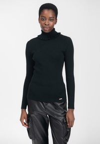 Top a collo alto nero a coste con un colletto arricciato, abbinato a pantaloni cargo in pelle nera. Presenta un marchio discreto sull'orlo.