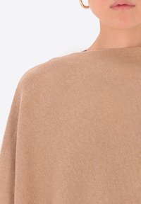 Maglione beige con una texture morbida, caratterizzato da una vestibilità ampia e un collo largo. Design semplice, dettagli minimi e una finitura liscia.