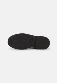 Semelle en caoutchouc noir texturé avec un design plat. Comprend un bord lisse et un détail de marque rectangulaire près du talon.