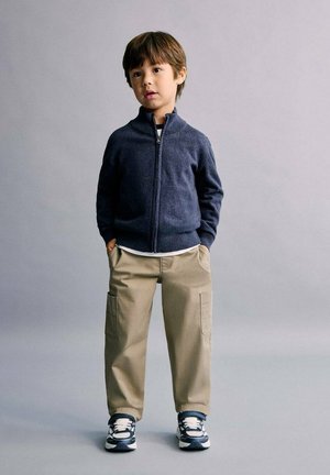 Pull zippé bleu marine sur une chemise blanche, pantalon cargo kaki et baskets bleu marine avec des accents blancs ; tenue décontractée pour un enfant.