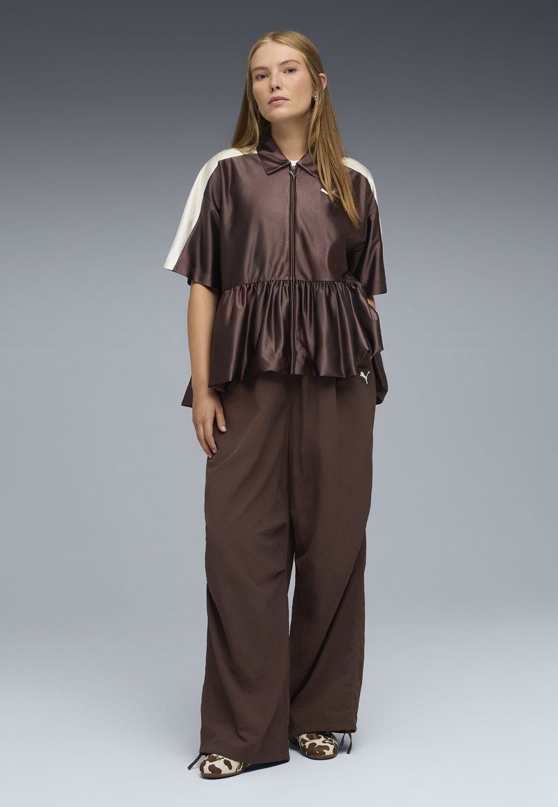Top in satin marrone con zip, design peplum, maniche crema. Abbinato a pantaloni marroni larghi e scarpe slip-on con stampa mucca.