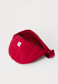 Borsa rossa imbottita con chiusura a zip e patch logo. Dotata di una tracolla regolabile e di una consistenza morbida, progettata per una facile conservazione.