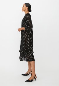 Czarna sukienka w kropki z złotymi akcentami, zwiewny materiał, rękawy do 3/4, warstwowy dół, w zestawie z czarnymi szpilkami typu slingback.