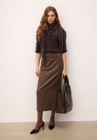 Rjav pulover iz volnene mešanice z gumbi, rjava prilegajoča krila, temnorjava usnjena torba in rjavih špicastih petah. Mat teksture, poenostavljena zasnova.