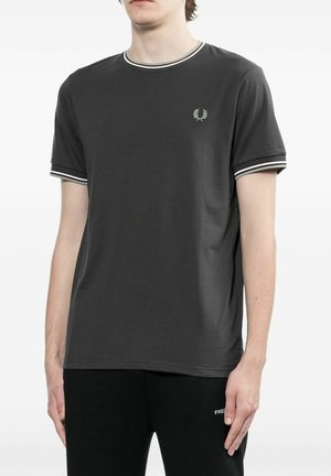 Modelo masculino con camiseta de manga corta gris oscuro con ribete a rayas blancas en el cuello y las mangas, combinada con pantalones negros.