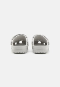Bílé dřeváky s hladkým plastovým povrchem, otevřeným zadním dílem a ventilačními otvory; strukturovaná podrážka pro přilnavost a pohodlí.