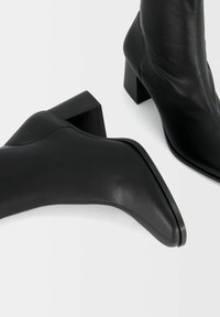 Czarne botki na kostkę wykonane z gładkiej skóry, charakteryzujące się spiczastym noskiem i masywnym obcasem typu blok o matowym wykończeniu.
