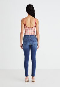 Top de malla a rayas rojas y blancas con tirantes finos, combinado con unos jeans ajustados azules que cuentan con bolsillos traseros y costuras mínimas.