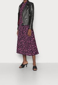 Giacca da motociclista in pelle nera sovrapposta a un vestito midi con stampa floreale rosa. Sandali con tacco aperti neri completano l'outfit.
