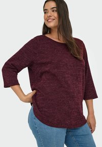 Top a maglia bordeaux con scollo rotondo e maniche a tre quarti, caratterizzato da un motivo testurizzato e un orlo curvo, abbinato a jeans blu.
