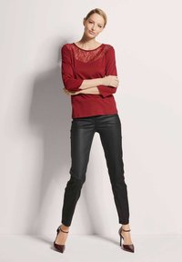 Bordeauxrode top met lange mouwen en kanten inzetstuk, gecombineerd met zwarte strakke broek en hoge hakken. Soepele textuur, eenvoudig ontwerp.