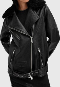 Μαύρο δερμάτινο μπουφάν μηχανής με γιακά από γούνα, πολλαπλές τσέπες με φερμουάρ, υφή ανάγλυφη και μέση με ζώνη.