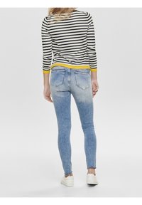 Randig långärmad topp i svart och vitt med gula accenter, kombinerad med ljusblå denim skinny jeans med en urtvättad finish och bakfickor.