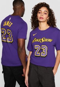 Fialové bavlněné trička s žlutými akcenty. Jedno má na zádech "JAMES" a "23"; druhé má na přední straně "LAKE SHOW" a "23".
