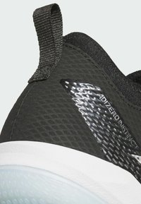 Black athletic shoe with a textured upper, white midsole, and glossy accent featuring "ADIZERO INSTINCT" branding. Includes a fabric heel tab.