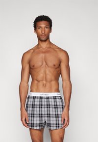 Pelēki un melni šaha raksta bokseršorti ar baltu Calvin Klein jostu, ar pogu aizdari un vieglu audumu.