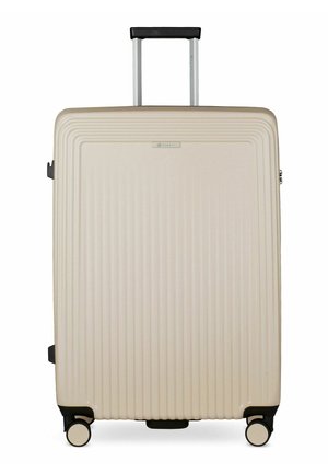 Grande valise rigide beige avec des rainures verticales, poignée noire étendue et quatre roulettes pivotantes noires et beiges sur fond blanc.