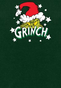 Camiseta verde con un dibujo del Grinch en un gorro de Santa rojo, con ojos amarillos y acentos blancos, rodeado de estrellas blancas.