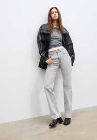 Crna kožna jakna, sivi prilagođeni top, svijetlosivi ravni traperice i crne čizme s potpeticama. Glatke teksture s minimalističkim dizajnom.