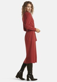 Red long-sleeve dress with a high collar, waist tie, and a smooth texture, paired with black knee-high heeled boots.