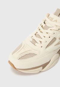 Krēmkrāsas sporta apavi ar zamšāda un sieta tekstūrām, ar bēšiem akcentiem, bieza auklām, noapaļotu purngalu un polsterētu zolīti.