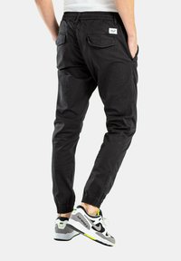 Schwarze Jogginghose mit elastischem Bund, seitlichen und hinteren Taschen, aus leichtem Stoff, kombiniert mit grauen und weißen Turnschuhen.