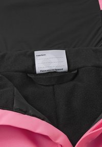 Das Innere der schwarzen und rosa Jacke verfügt über ein weiches Fleece-Futter, eine satinierte Oberfläche und ein Pflegeetikett mit Anweisungen sowie einer Botschaft, sie weiterzugeben.