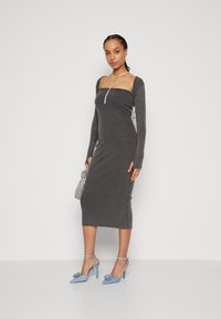 Robe midi grise à côtes avec des manches longues, décolleté carré, fermeture éclair sur le devant et détails froncés sur le côté. Associée à des escarpins pointus bleu clair.